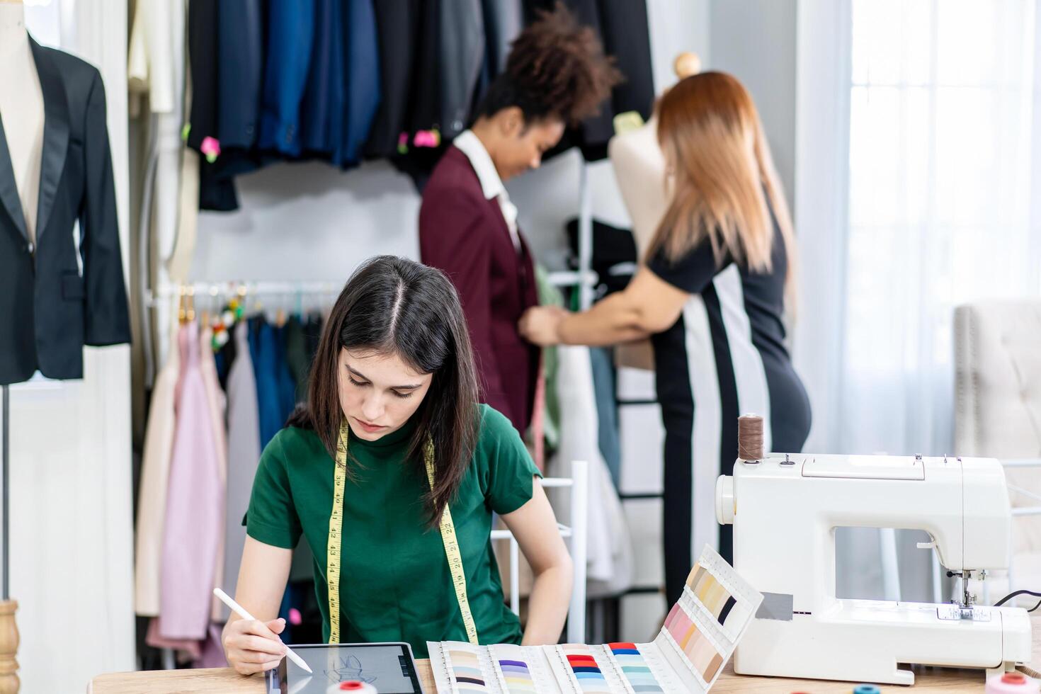 Caucasian female fashion designer works in studio by idea drawing sketches with digital tablet and colorful fabric for a dress design collection, choose clothing colors for tailoring and designing photo
