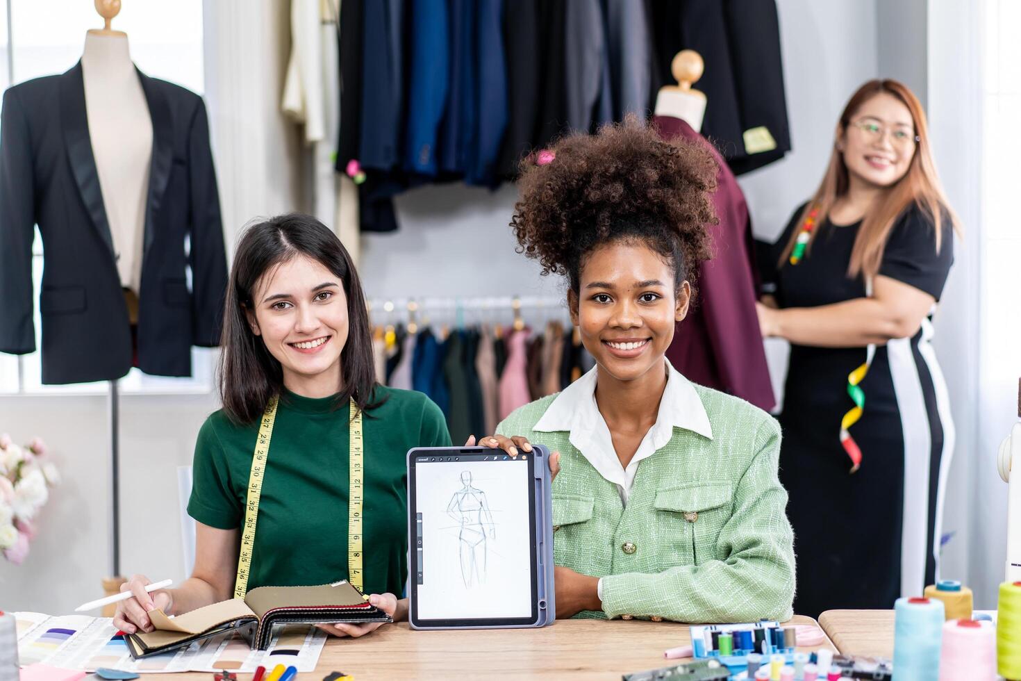 Young two fashion designers use digital tablet meeting with graphic designer discuss show sample dress design new collection on screen on desk while working in sewing workshop photo