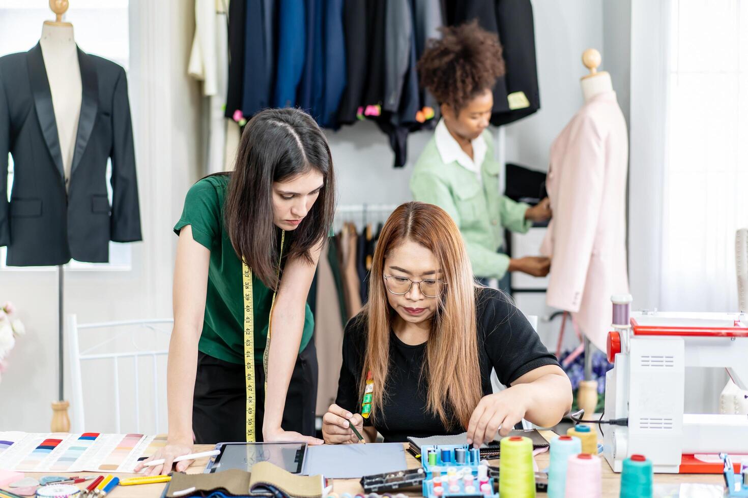 Team of three fashion designers preparation for create new clothes collection in workshop studio and tablet for checking with sample fabric colors, They talking about clothing design at work place. photo