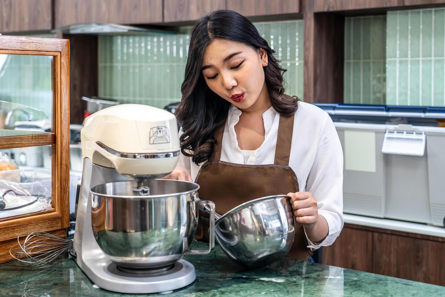 Young asian women i s shop owner Put on an apron making cream for cupcakes, Using electric mixer, Preparing Cookies, Cooking, Homemade, Made specifically to sell photo