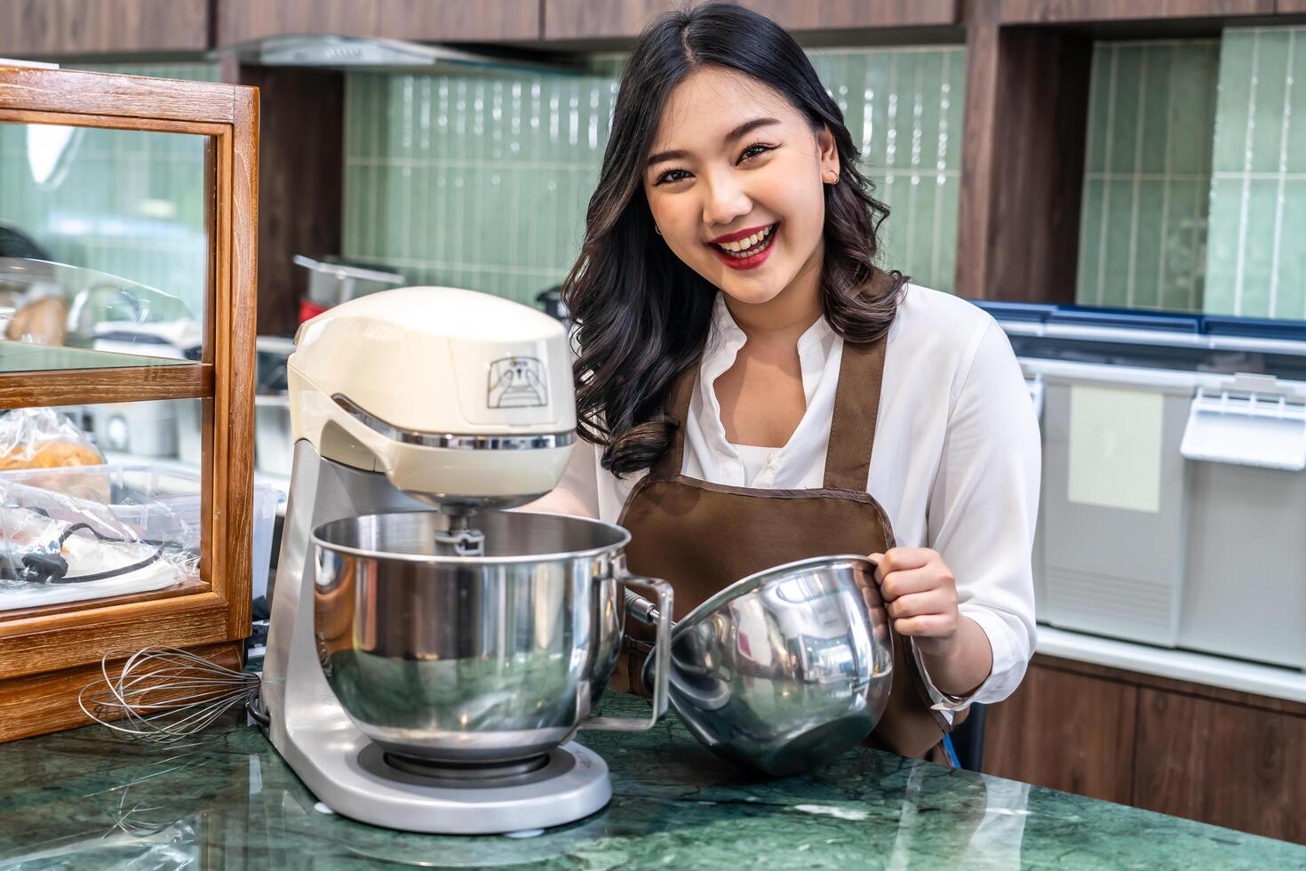 Young asian women i s shop owner Put on an apron making cream for cupcakes, Using electric mixer, Preparing Cookies, Cooking, Homemade, Made specifically to sell photo