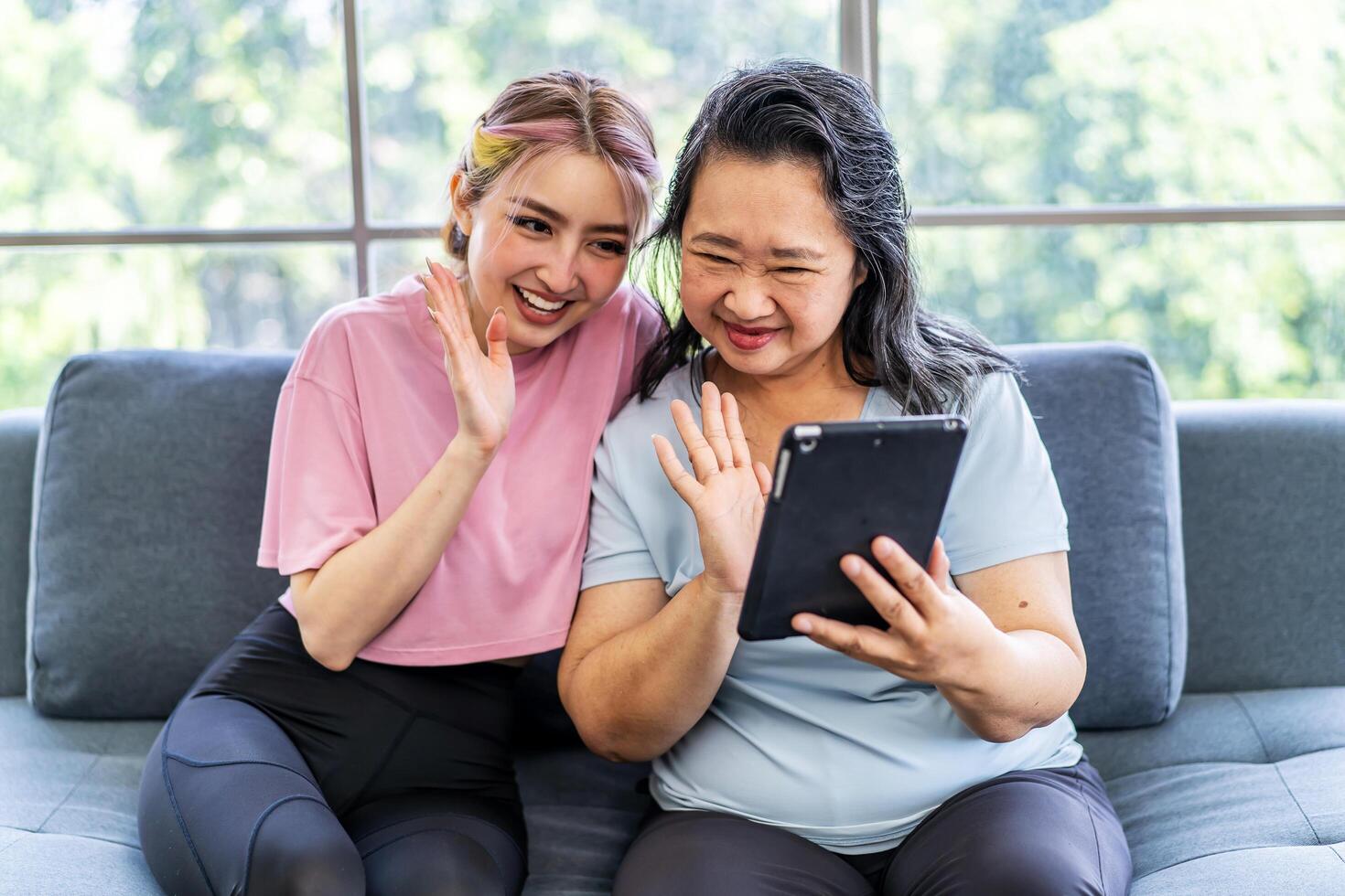 Happy senior asian mother and young daughter waving hands looking at web camera using tablet for call, smiling mom and girl having fun greeting online by computer webcam making videocall photo