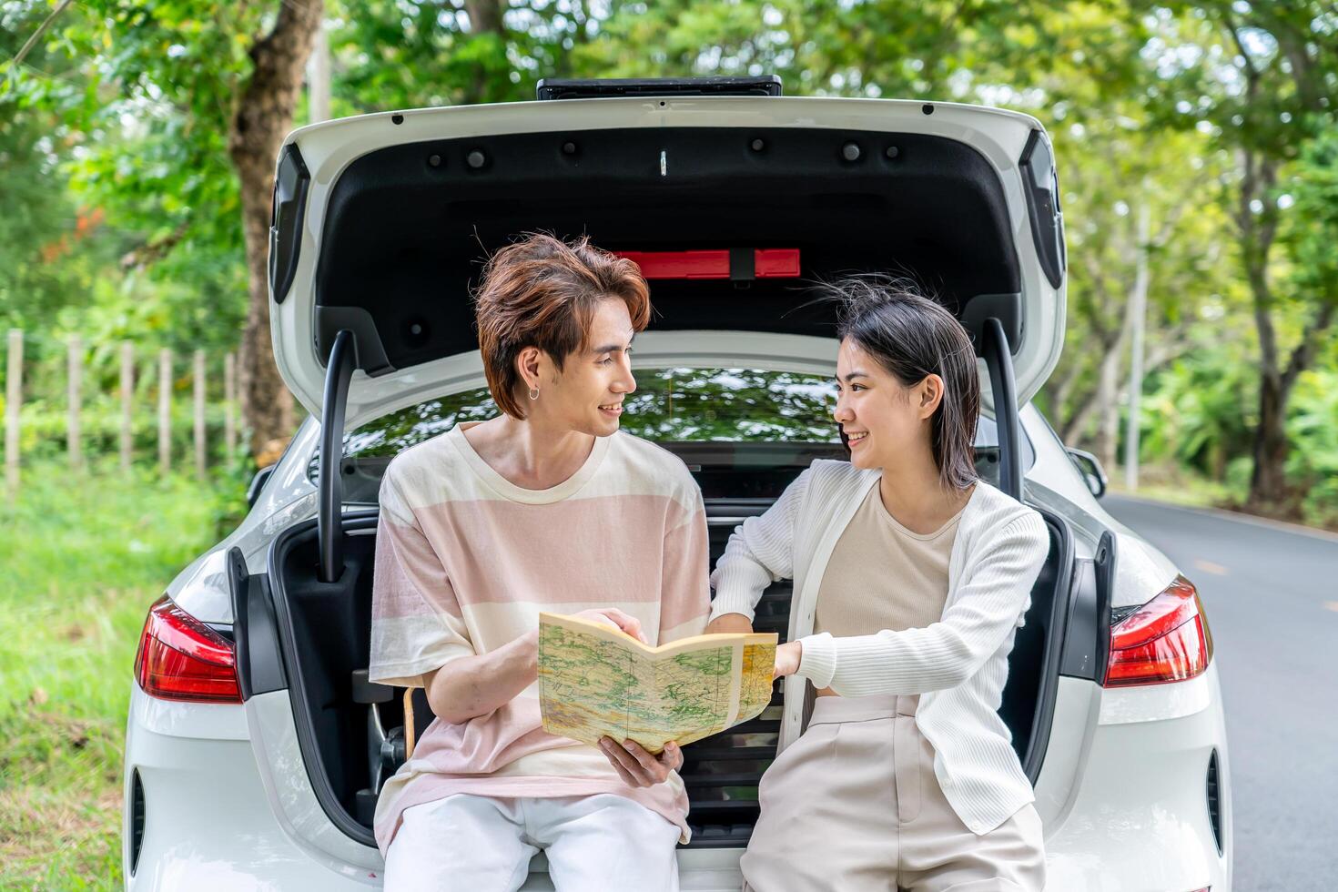 Traveler couple on road trip, man and woman sitting together in car trunk using map on journey during the trip, Two young boy and girl travel, Two friend traveling on vacation, searching road in map photo