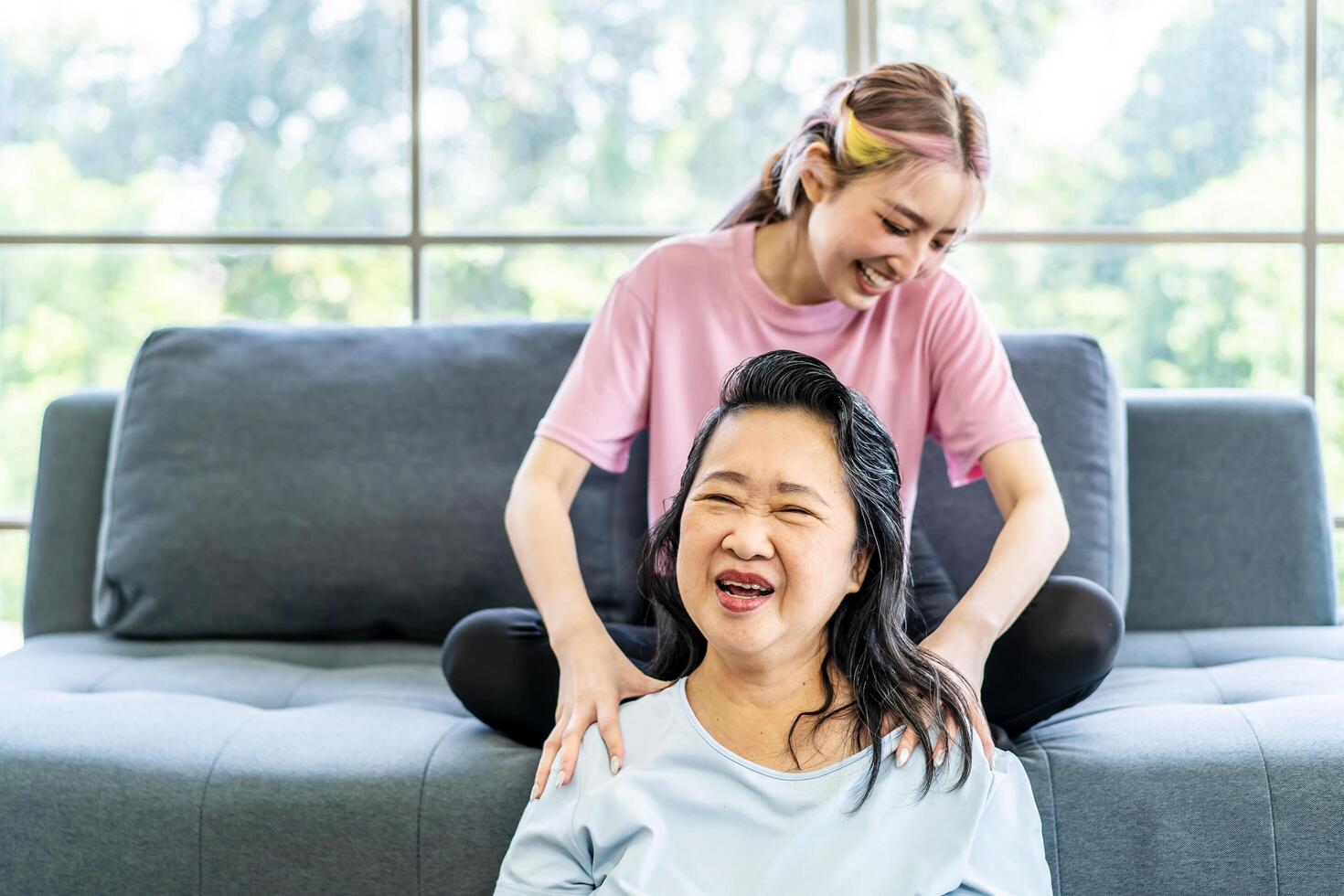 Young Asian daughter massages shoulder, relieves pain of elderly Asian mother while sitting on the sofa at home, Family concept. Health care. Chronic shoulder pain treatment photo