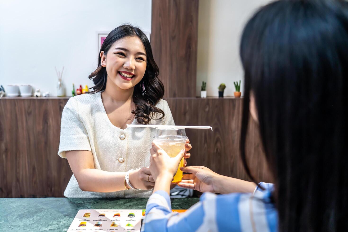 Waiter serving glass of fresh juice to a customer who was a young asian woman on counter in the restaurant, Juice bar employees serving drink to customer, good service, Good-natured atmosphere photo