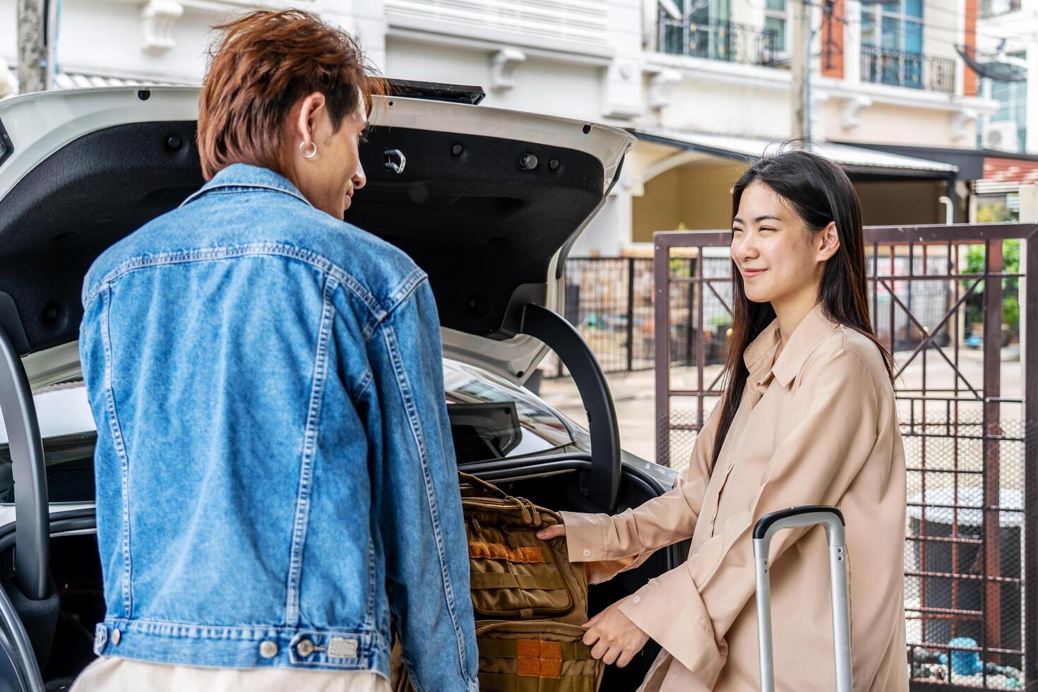 Couple young asian man and woman tourist puts his backpack suitcase package luggage in the car boot trunk. Preparing for vacation. Loading a car for a sstkroadtrip. Travel. Summer adventure photo