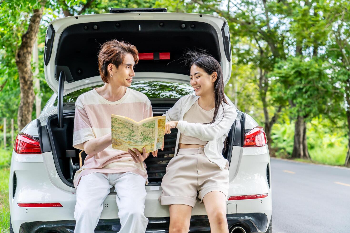 Traveler couple on road trip, man and woman sitting together in car trunk using map on journey during the trip, Two young boy and girl travel, Two friend traveling on vacation, searching road in map photo