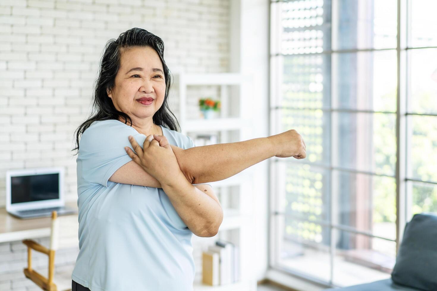 Morning work-out, Senior asian woman doing fitness exercises from home, Fitness woman doing stretch exercise stretching her arms, Elderly woman living an active lifestyle. photo
