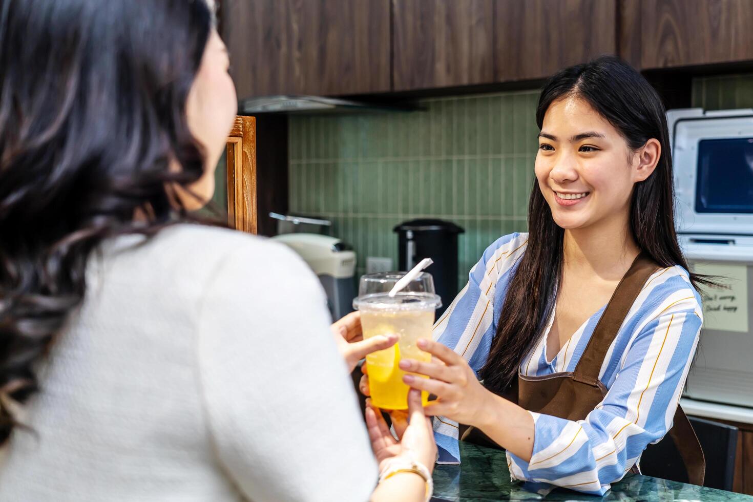 Smiling young asian waitress in a cafe with customer for service, payment or order on counter at coffee shop. Serving, employee in small business restaurant helping a girl client at checkout or work photo