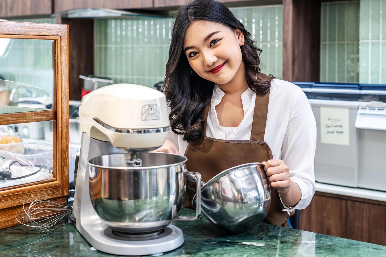 Young asian women i s shop owner Put on an apron making cream for cupcakes, Using electric mixer, Preparing Cookies, Cooking, Homemade, Made specifically to sell photo