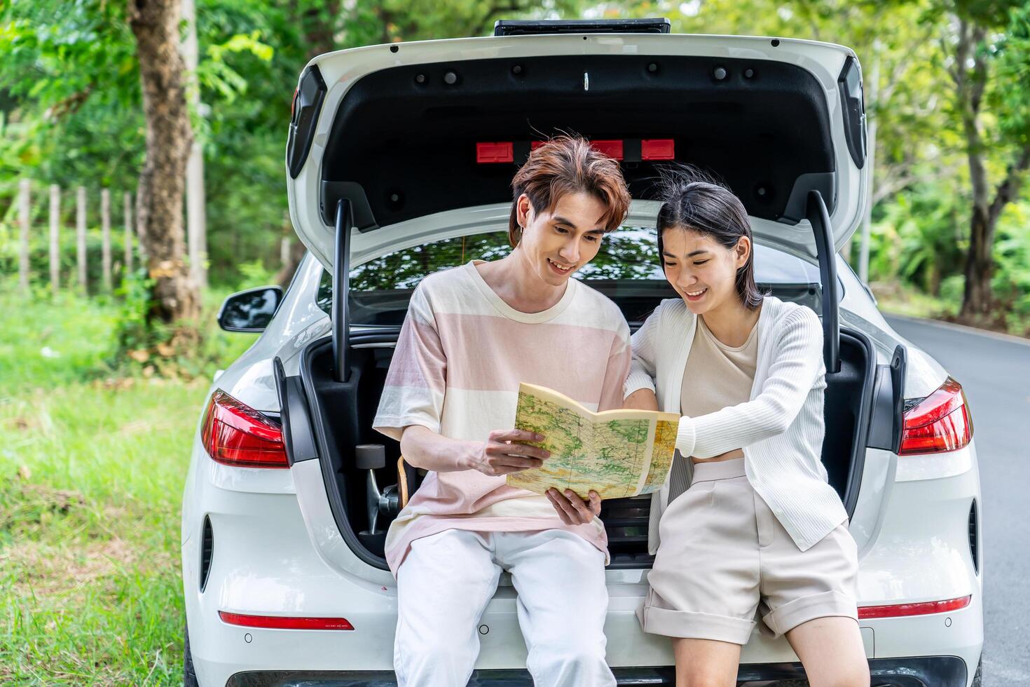 Traveler couple on road trip, man and woman sitting together in car trunk using map on journey during the trip, Two young boy and girl travel, Two friend traveling on vacation, searching road in map photo