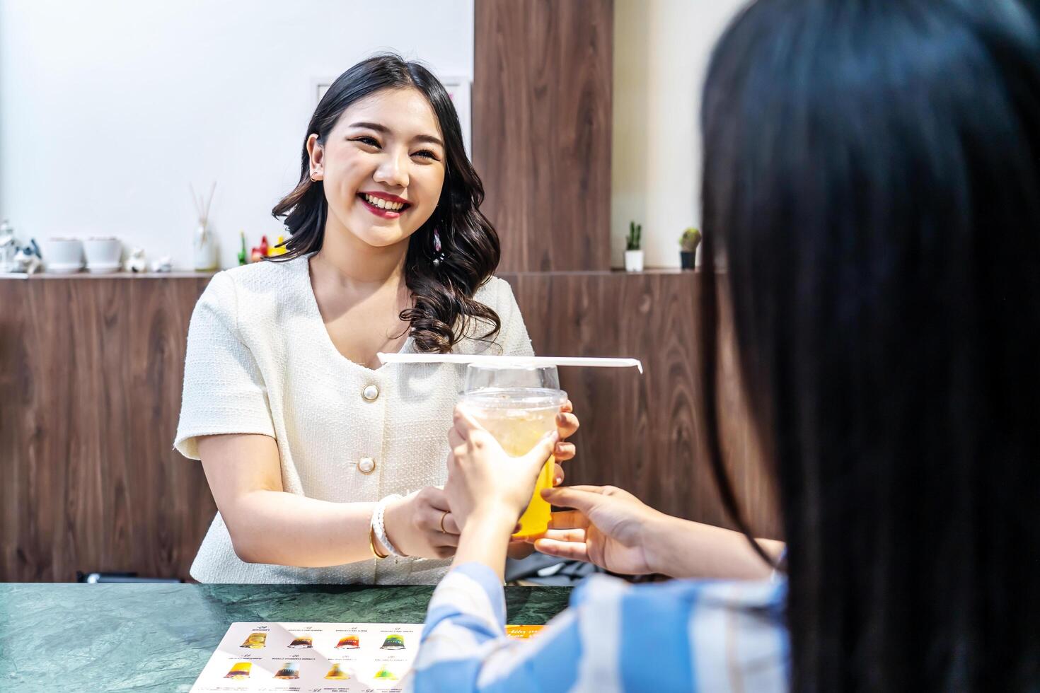 Waiter serving glass of fresh juice to a customer who was a young asian woman on counter in the restaurant, Juice bar employees serving drink to customer, good service, Good-natured atmosphere photo