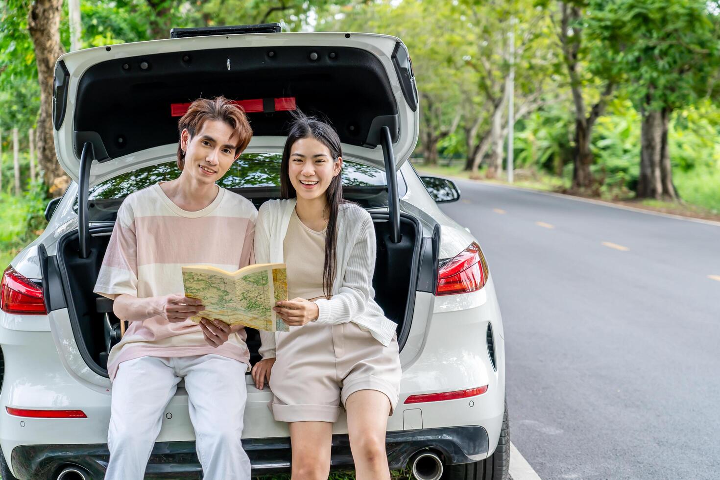 Traveler couple on road trip, man and woman sitting together in car trunk using map on journey during the trip, Two young boy and girl travel, Two friend traveling on vacation, searching road in map photo
