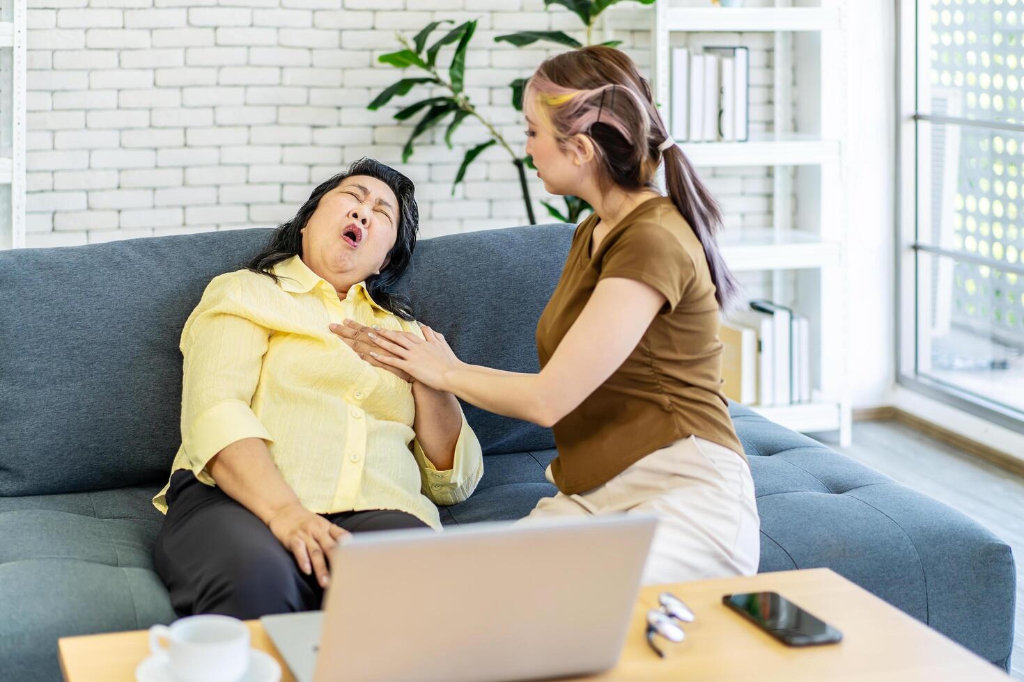Elderly asian woman having chest pain or heart attack, clutching and having difficult breathing, Loving daughter take care of elderly mother while having left chest pain on sofa. photo