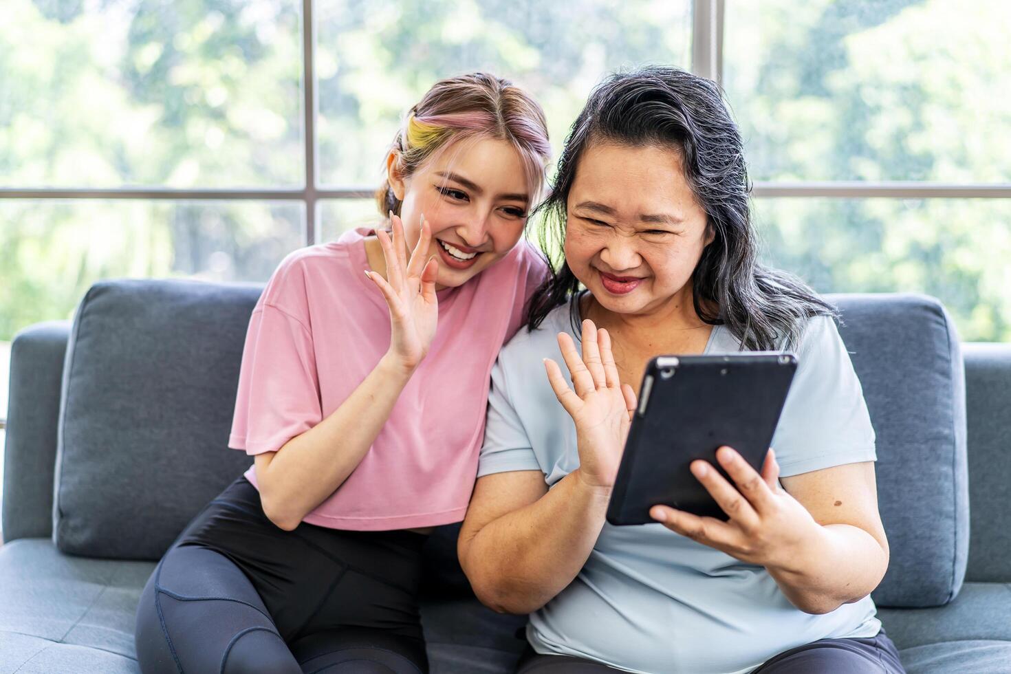 Happy senior asian mother and young daughter waving hands looking at web camera using tablet for call, smiling mom and girl having fun greeting online by computer webcam making call photo