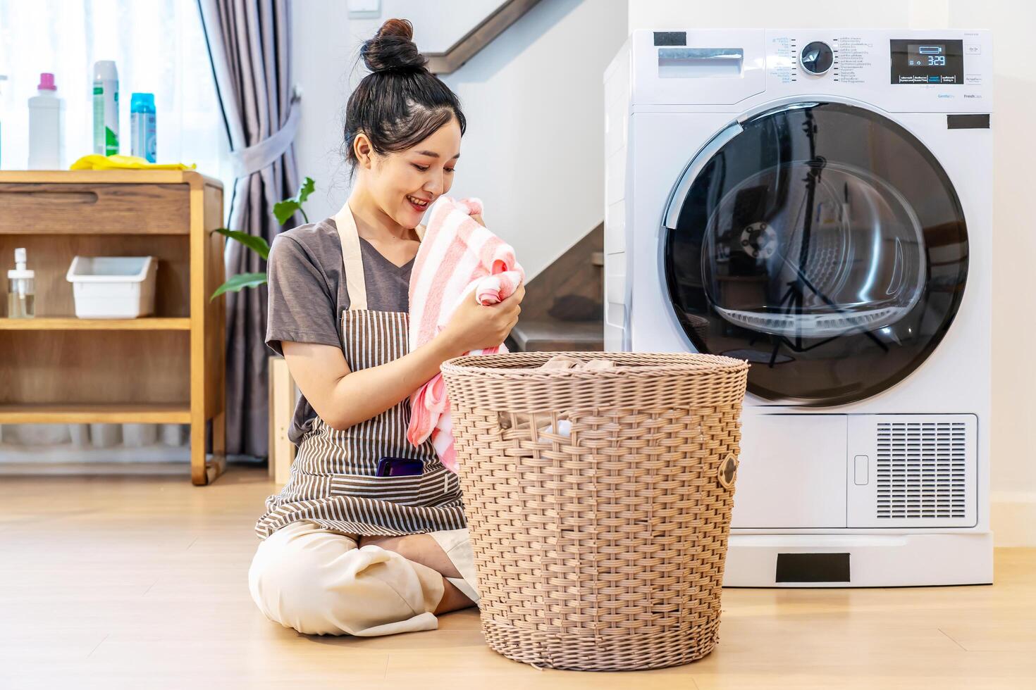 Smell, smile young asian woman doing fresh laundry from the washing machine in home. Happy girl and a home cleaner smelling a towel or clothes from the wash for happiness and housekeeping photo