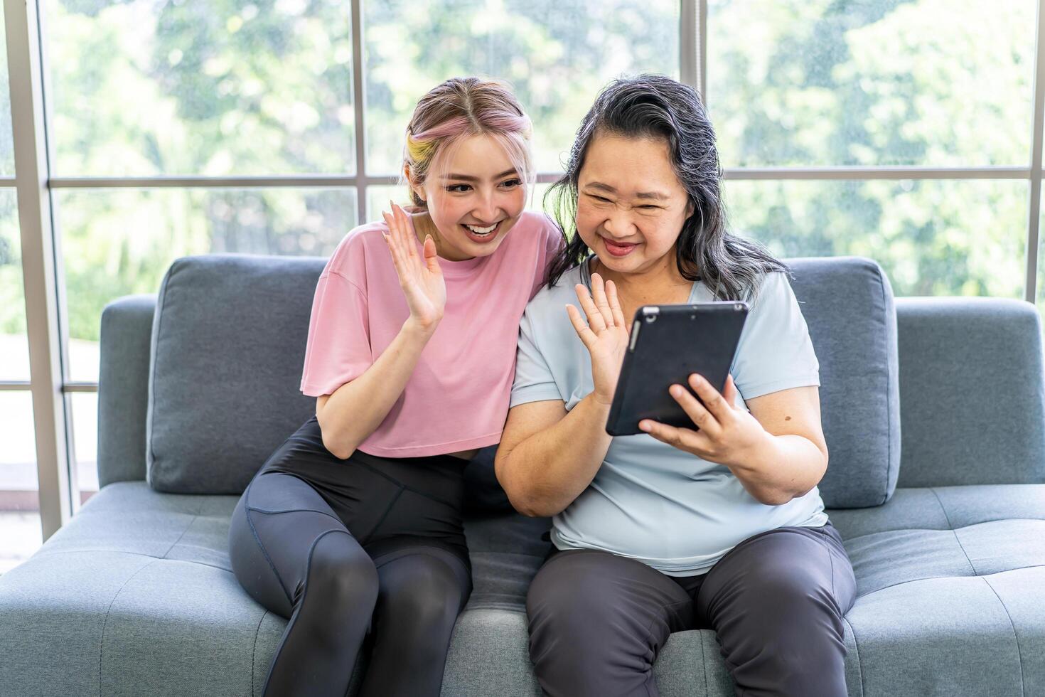 Happy senior asian mother and young daughter waving hands looking at web camera using tablet for call, smiling mom and girl having fun greeting online by computer webcam making videocall photo