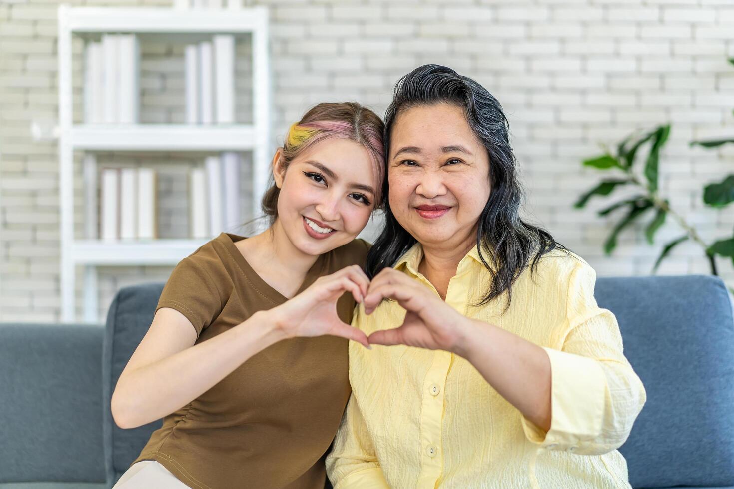 In truth, a family is what you make it. Shot of happy smiling asian senior mother and daughter making a heart sign with their hands at home, family enjoying leisure time photo