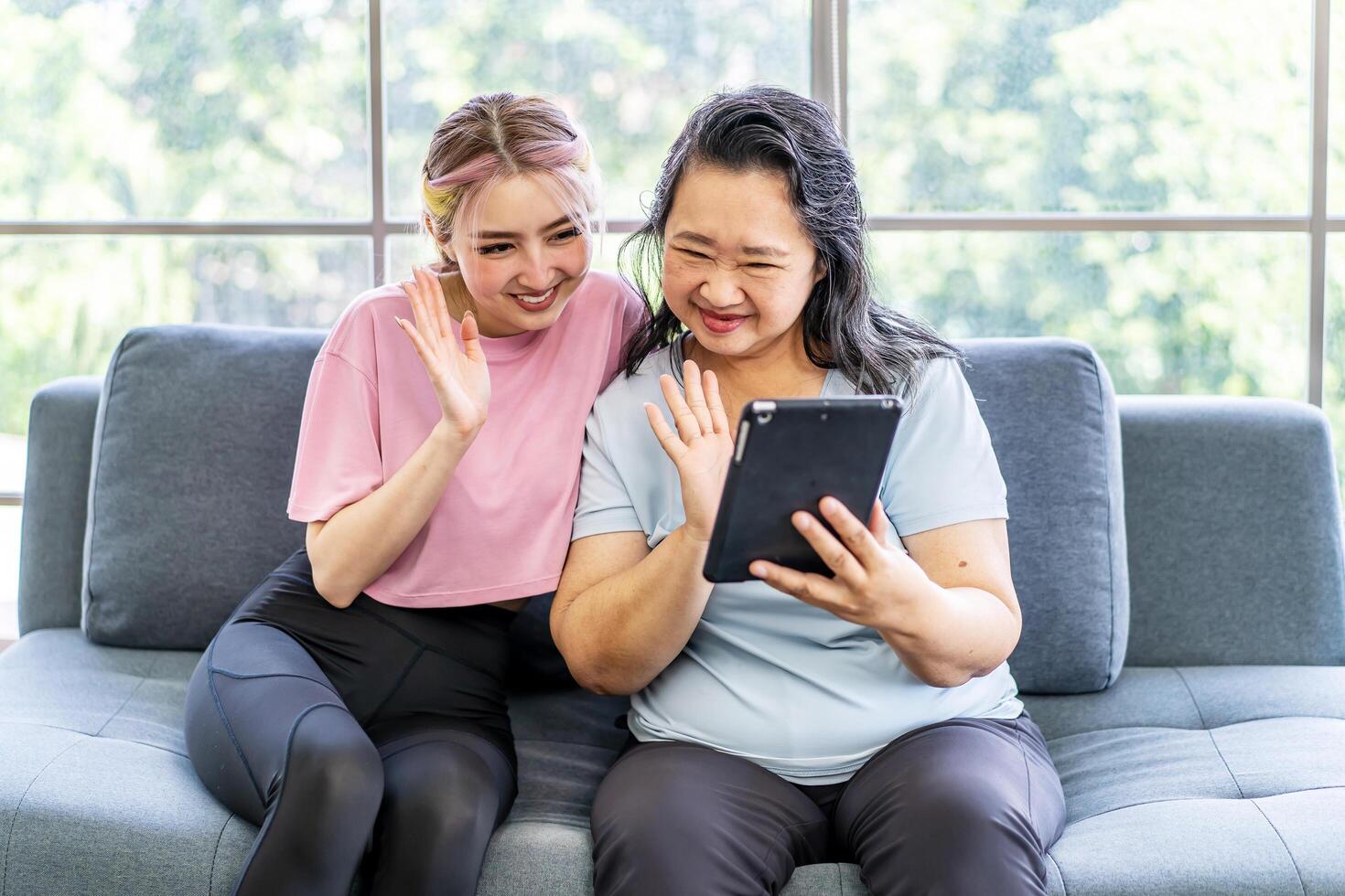 Happy senior asian mother and young daughter waving hands looking at web camera using tablet for call, smiling mom and girl having fun greeting online by computer webcam making videocall photo