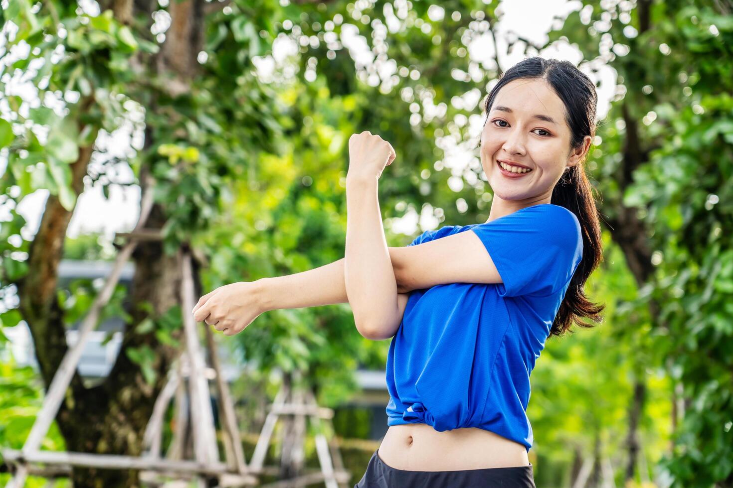Strong athletic asian woman stretching warming up before running. Fit sport girl stretching her body warm up before workout outdoor. The girl in sportswear exercises outside for health and wellbeing photo