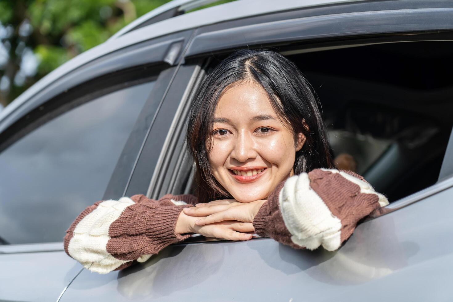 Happy cute asian woman enjoying the breeze sitting in a car looking out of the window's car while having a road trip watching a beautiful sunset tree view, Driving road trip on vacation photo