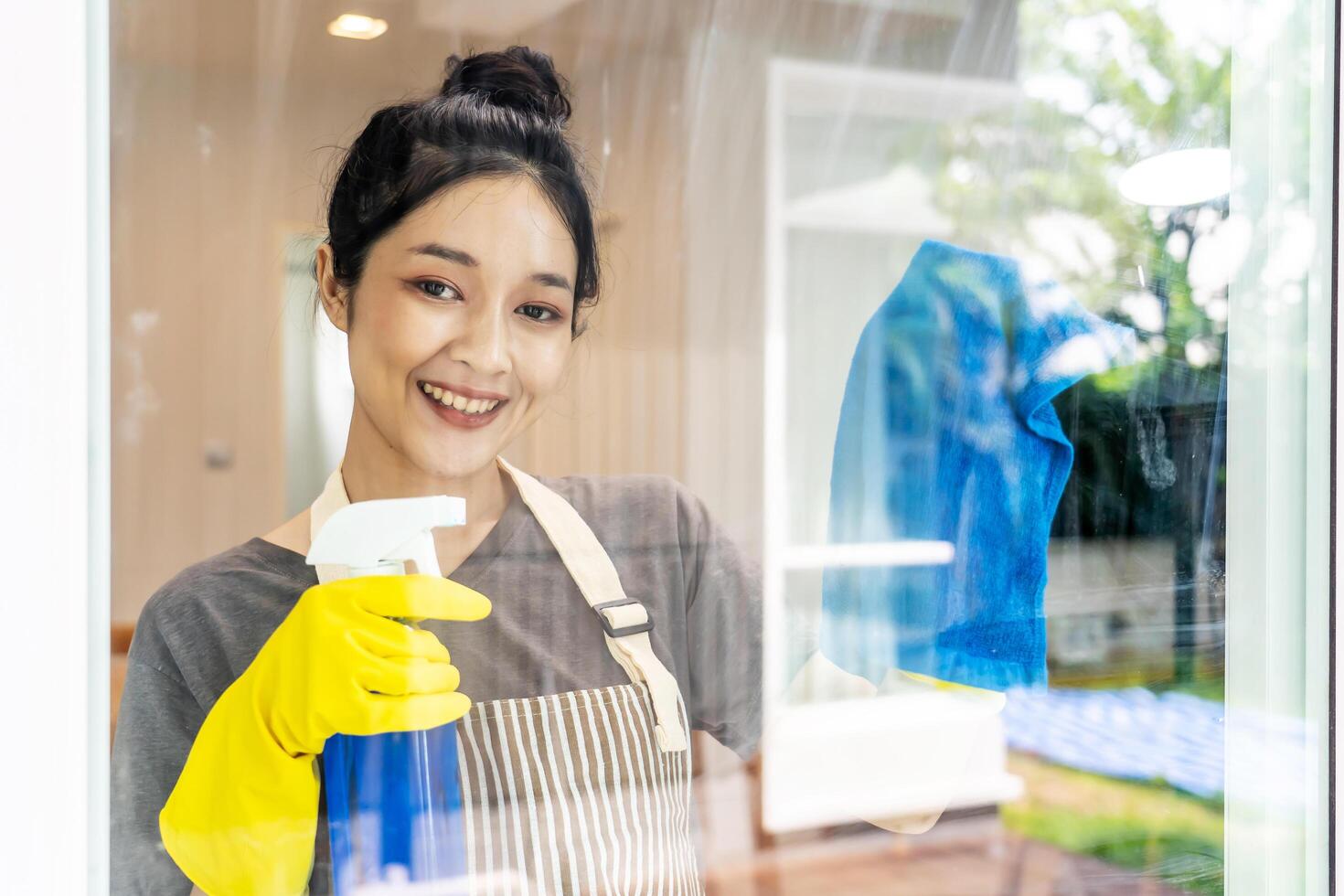 Portrait of cheerful positive young woman asian in yellow protective rubber gloves cleaning window with rag and cleanser spray at home, enjoying housework, happily performing domestic chores photo