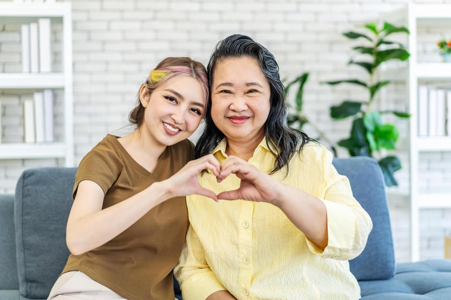 In truth, a family is what you make it. Shot of happy smiling asian senior mother and daughter making a heart sign with their hands at home, family enjoying leisure time photo