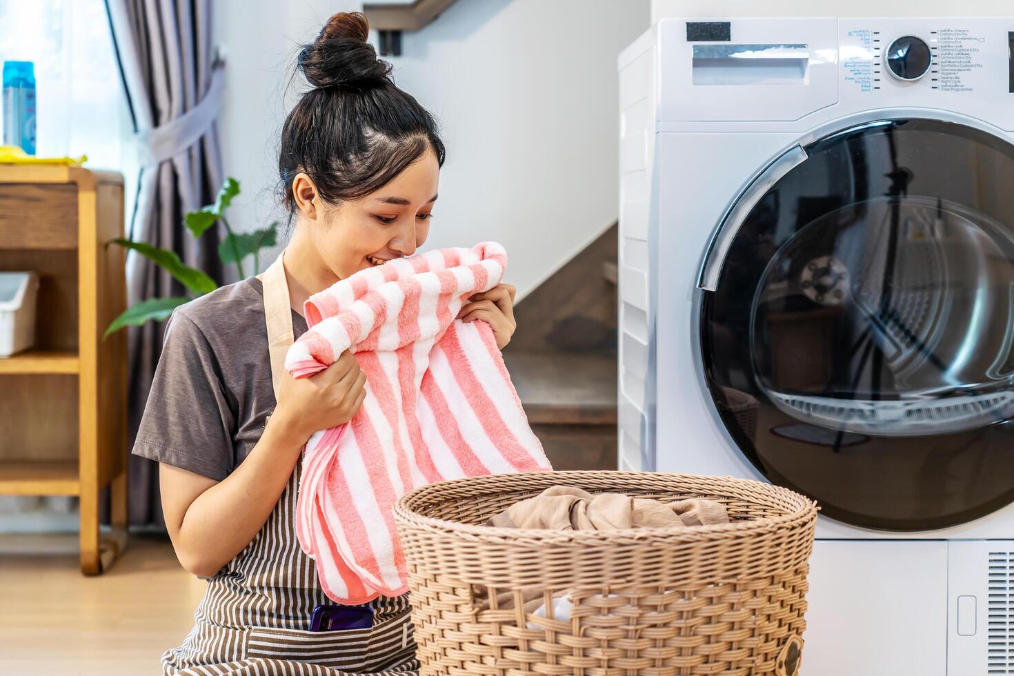 Smell, smile young asian woman doing fresh laundry from the washing machine in home. Happy girl and a home cleaner smelling a towel or clothes from the wash for happiness and housekeeping photo