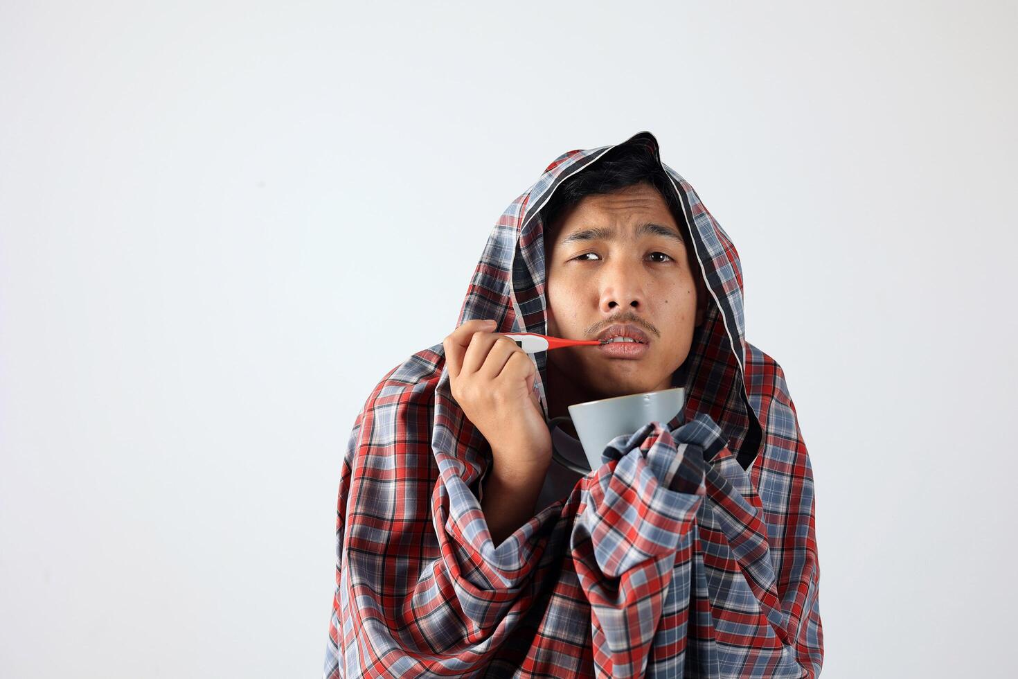Ill Man Covered with Sarung Holding a Tea Cup and Thermometer photo
