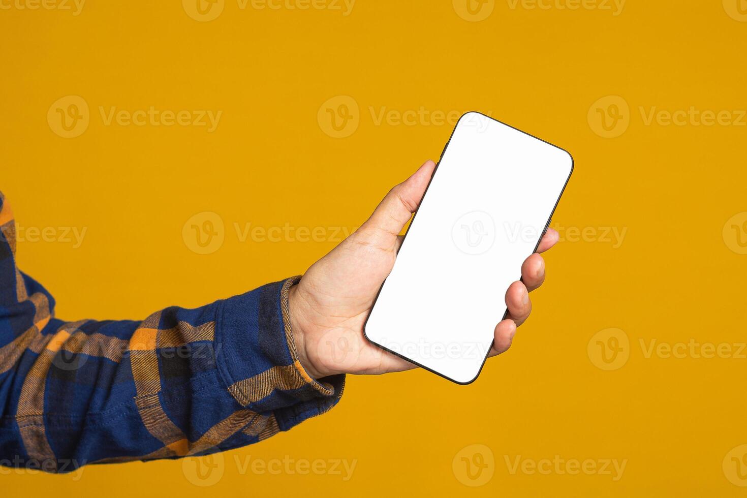 Technology, communication, and advertising concept. Close-up of hand holding a mobile phone with blank copy space screen for text message or information while standing with a yellow background photo