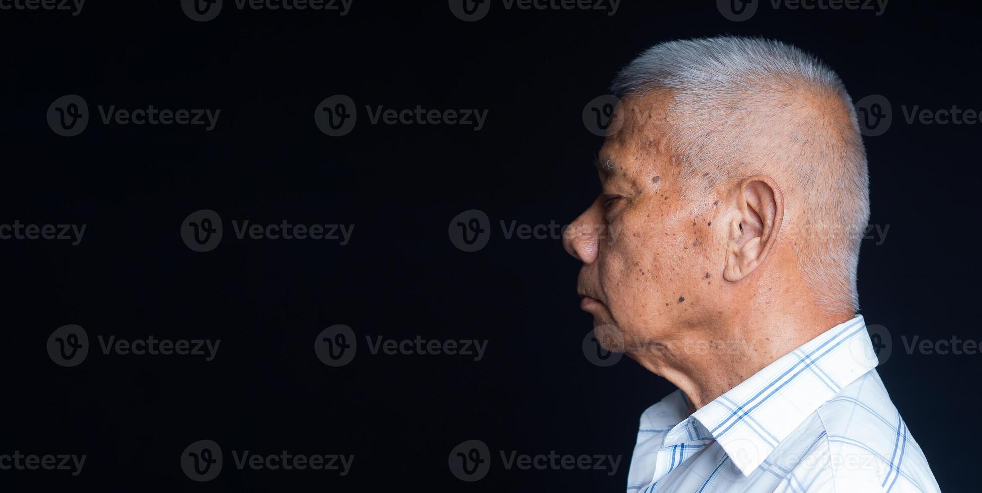 Side view of a senior man in a white shirt eyes closed while standing on a black background in the studio photo