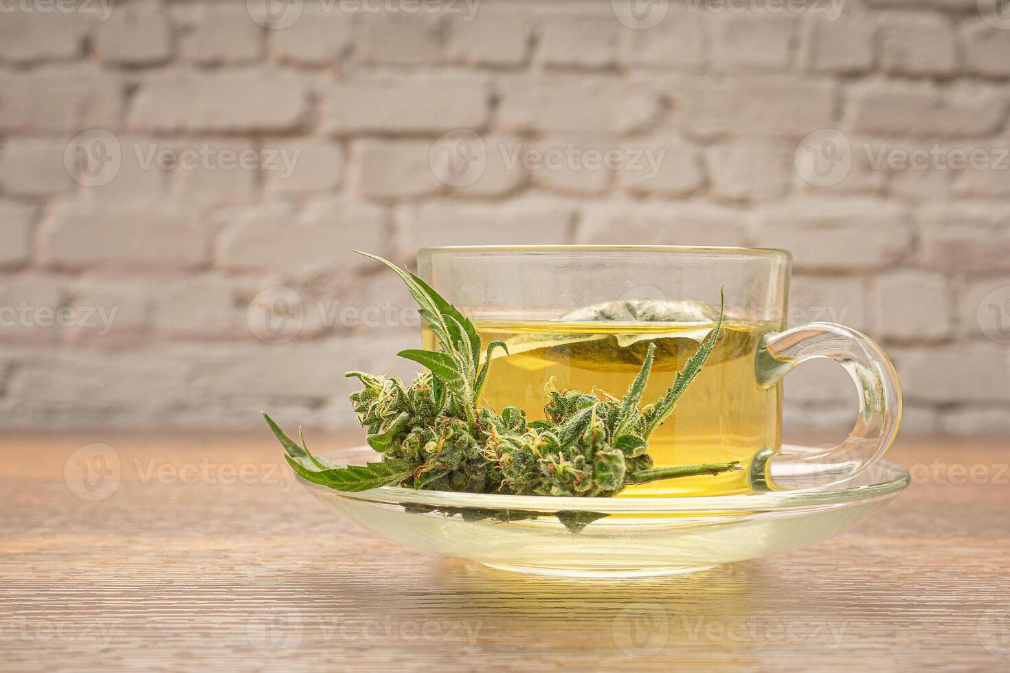 Cannabis tea in a teacup and marijuana buds flower isolated on a wooden table with white brick background photo