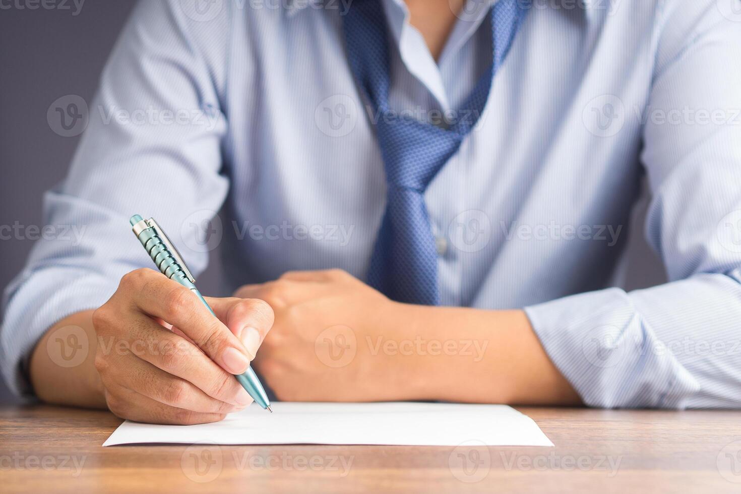 Close-up of a businessman holding a pen writing on paper on a wooden desk while sitting on a chair in the office. Space for text. Business and relaxation concept photo