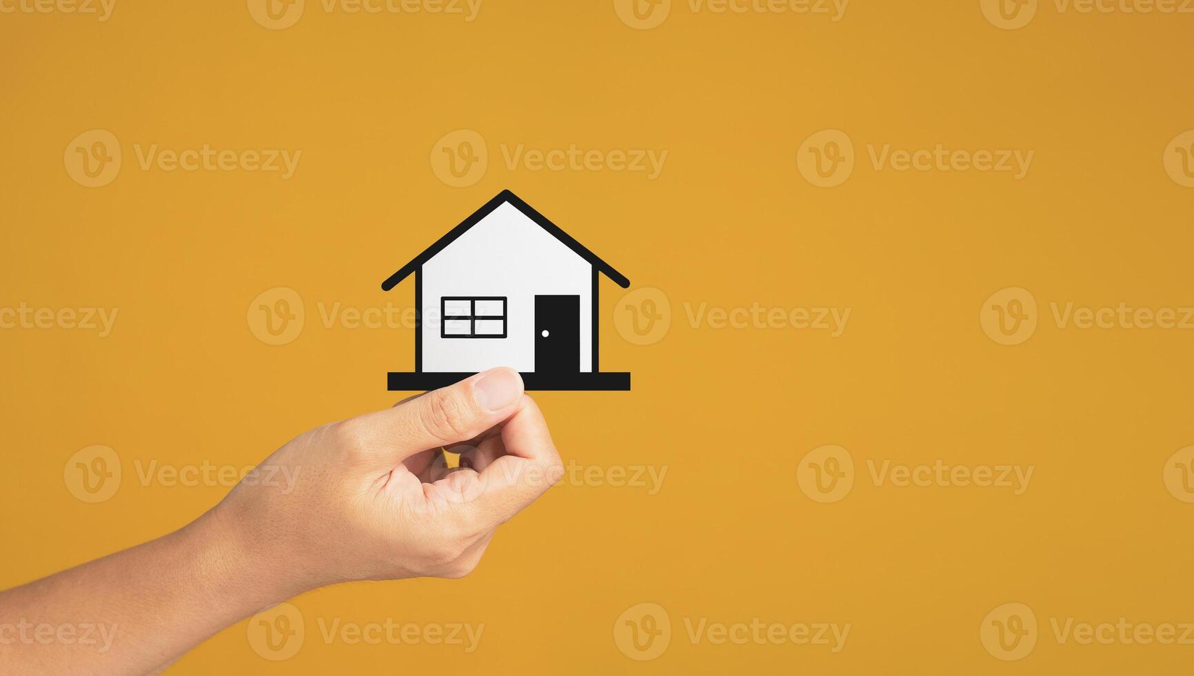 Business and real estate concept. Close-up of hand holding a mini paper house while standing on a yellow background in the studio. Space for text. Property insurance and security photo