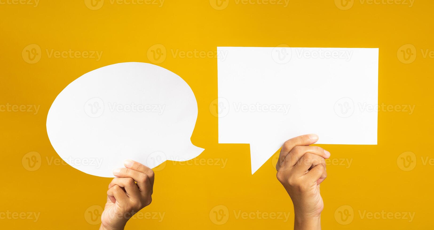 Speech bubble concept. Close-up of hands holding of two empty white speech balloons are over a yellow background with copy space for text photo