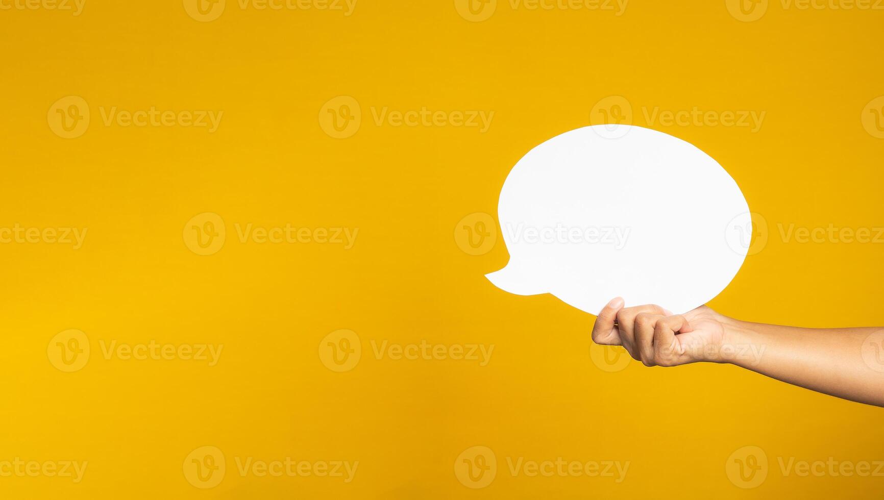 A speech bubble concept. Hand holding of an empty white speech balloon on yellow background with copy space for text. Close-up photo