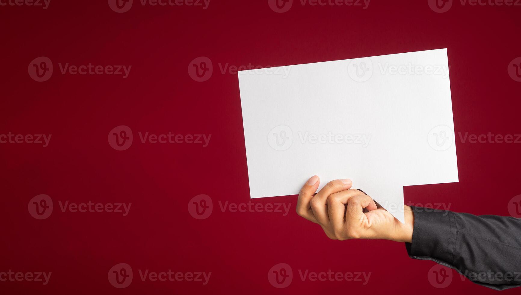 A speech bubble concept. Hand holding an empty white speech bubble over on a red background with copy space for text. Close-up photo