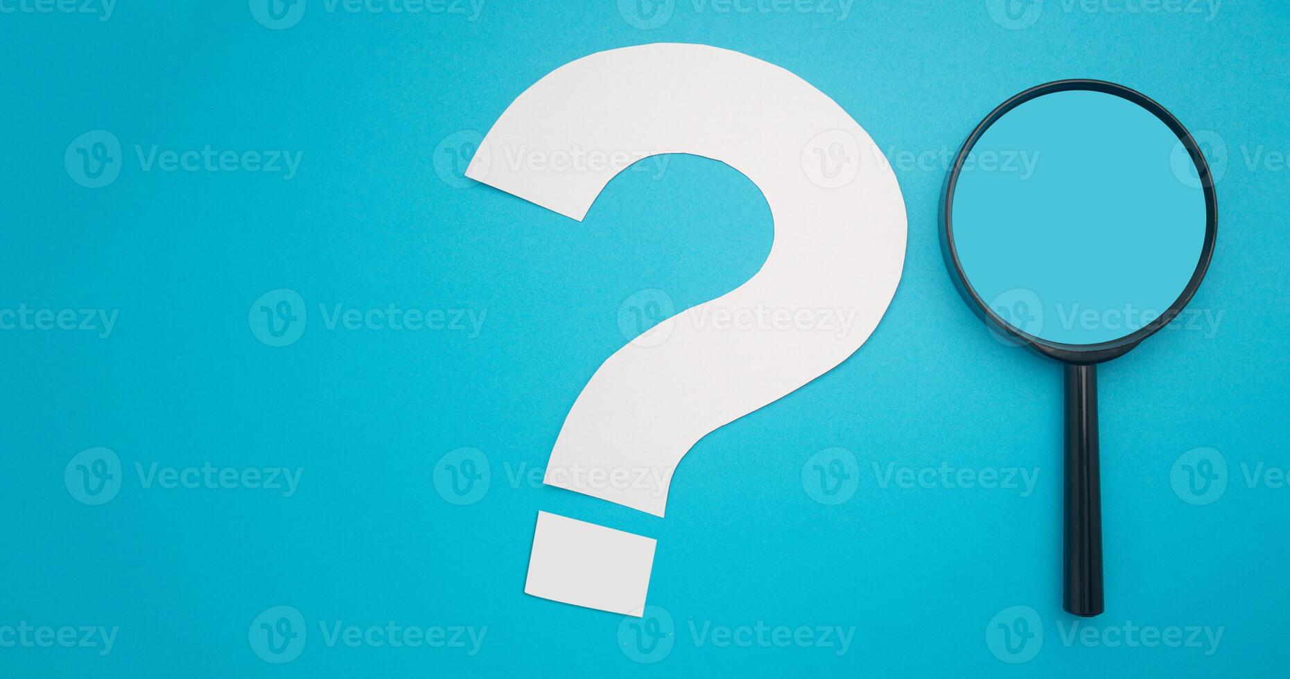 A magnifying glass and a white question mark symbol are on a blue background. Search and question mark concept. Top view. Space for text photo