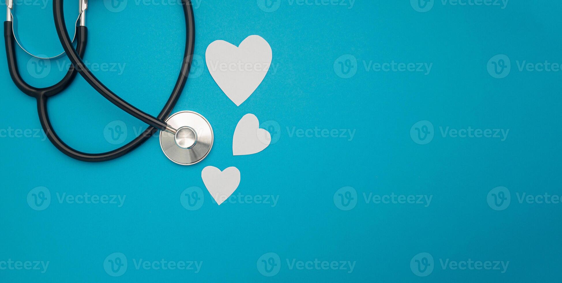 Top view of a stethoscope with white heart paper shape on a blue background. Space for text. Medical and healthcare concept photo