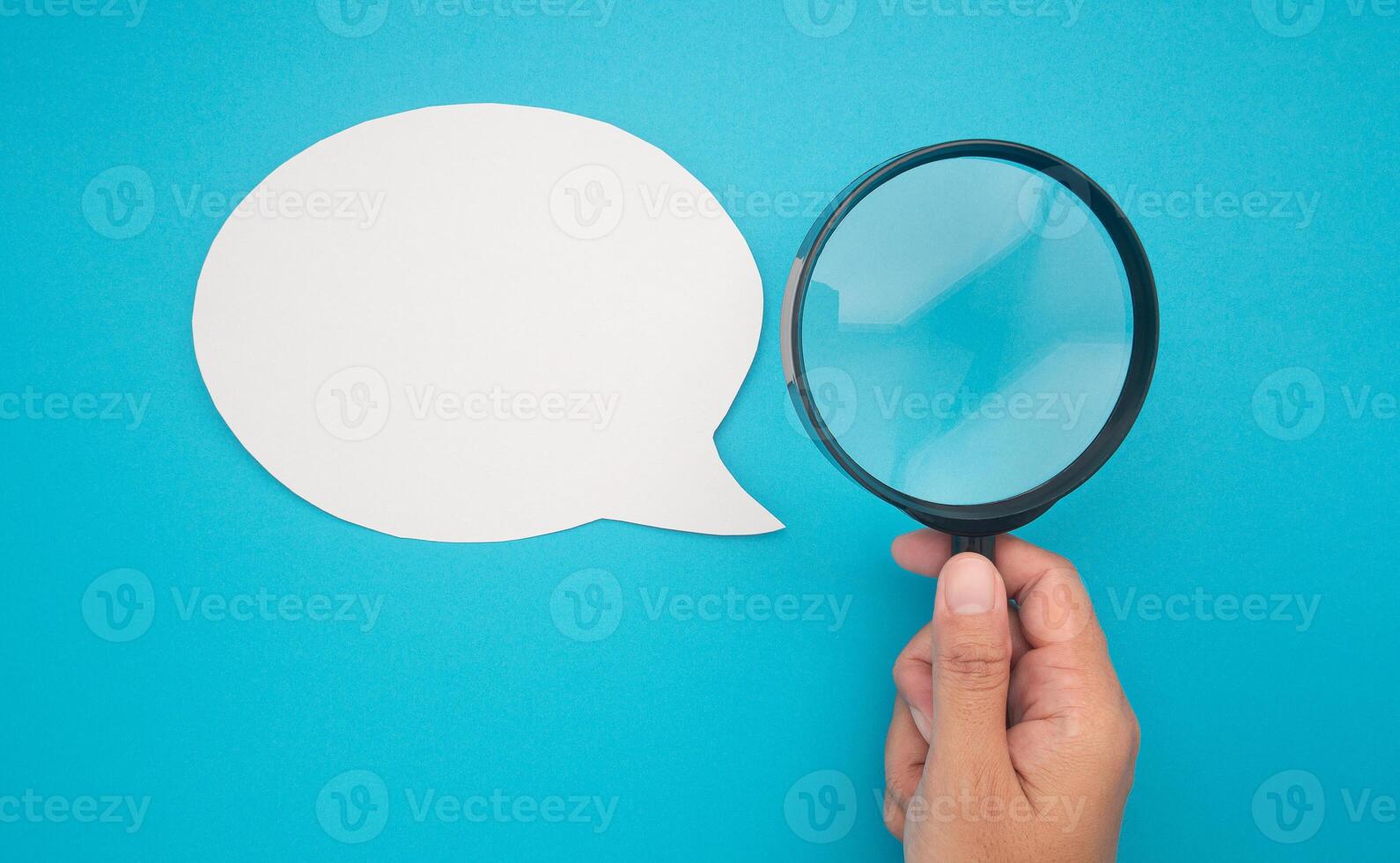 Top view of a blank white speech bubble and hand holding a magnifying glass on a blue background photo