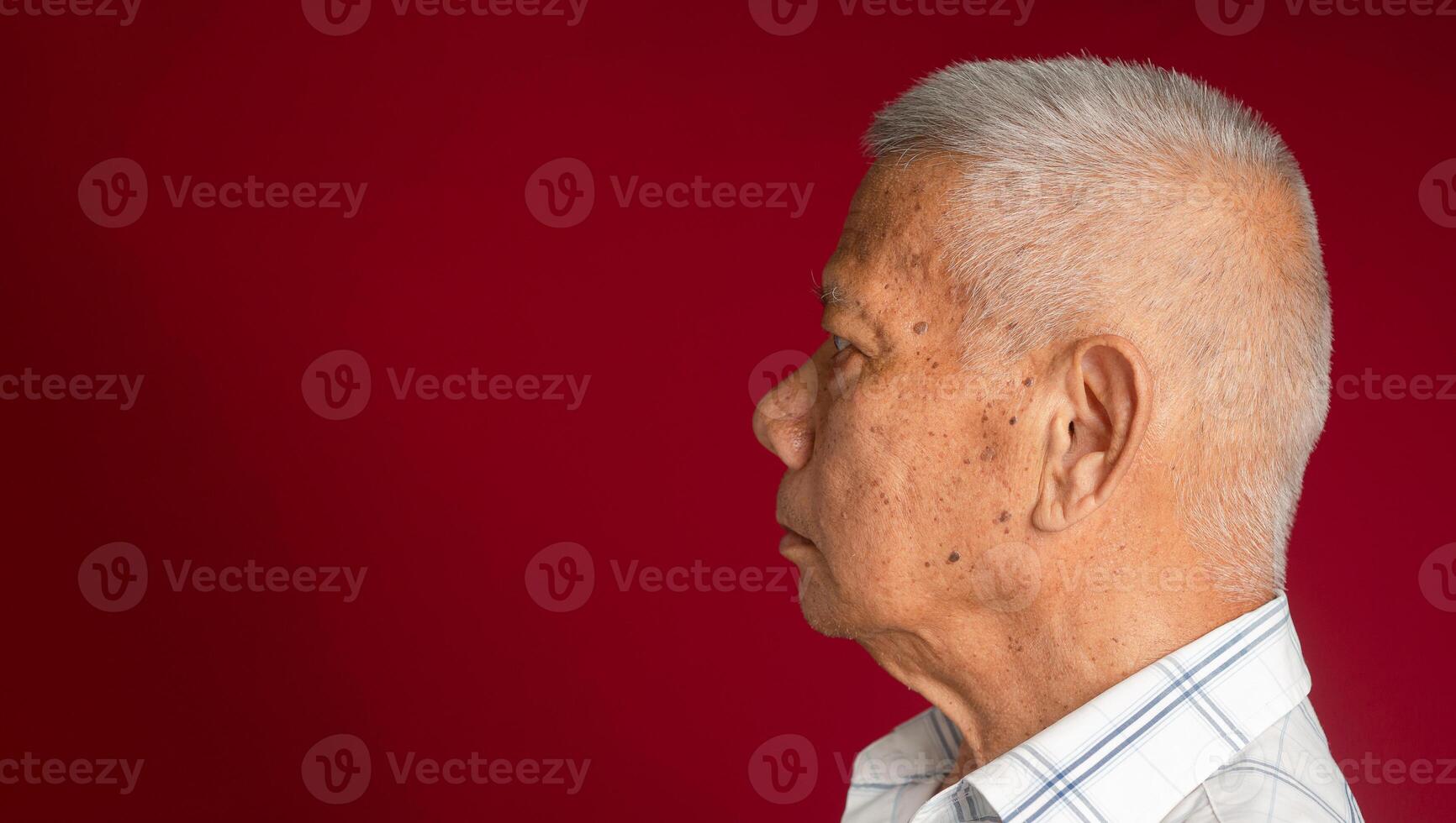 Side view of an elderly Asian man looking away while standing on a red background in the studio. Space for text. Aged people and healthcare concept photo