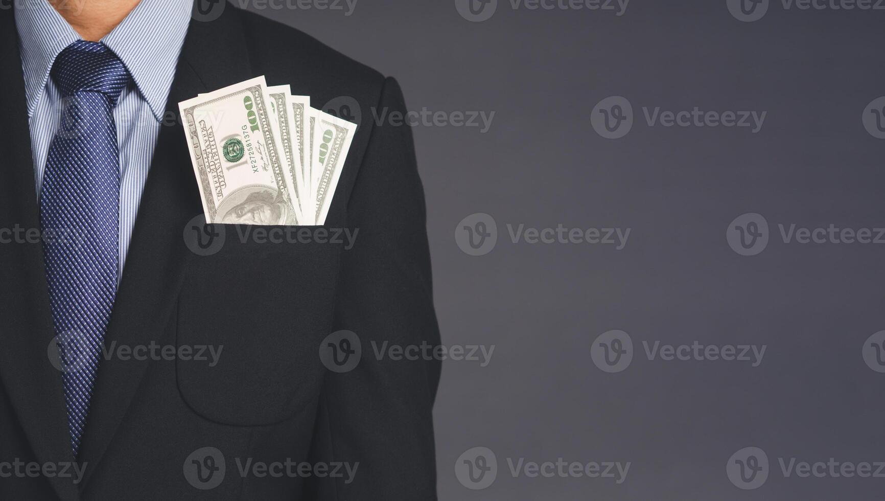 Business, finance, payday loan concept. Businessman wearing a suit with US dollar banknotes in a suit pocket while standing with a gray background with space for text photo