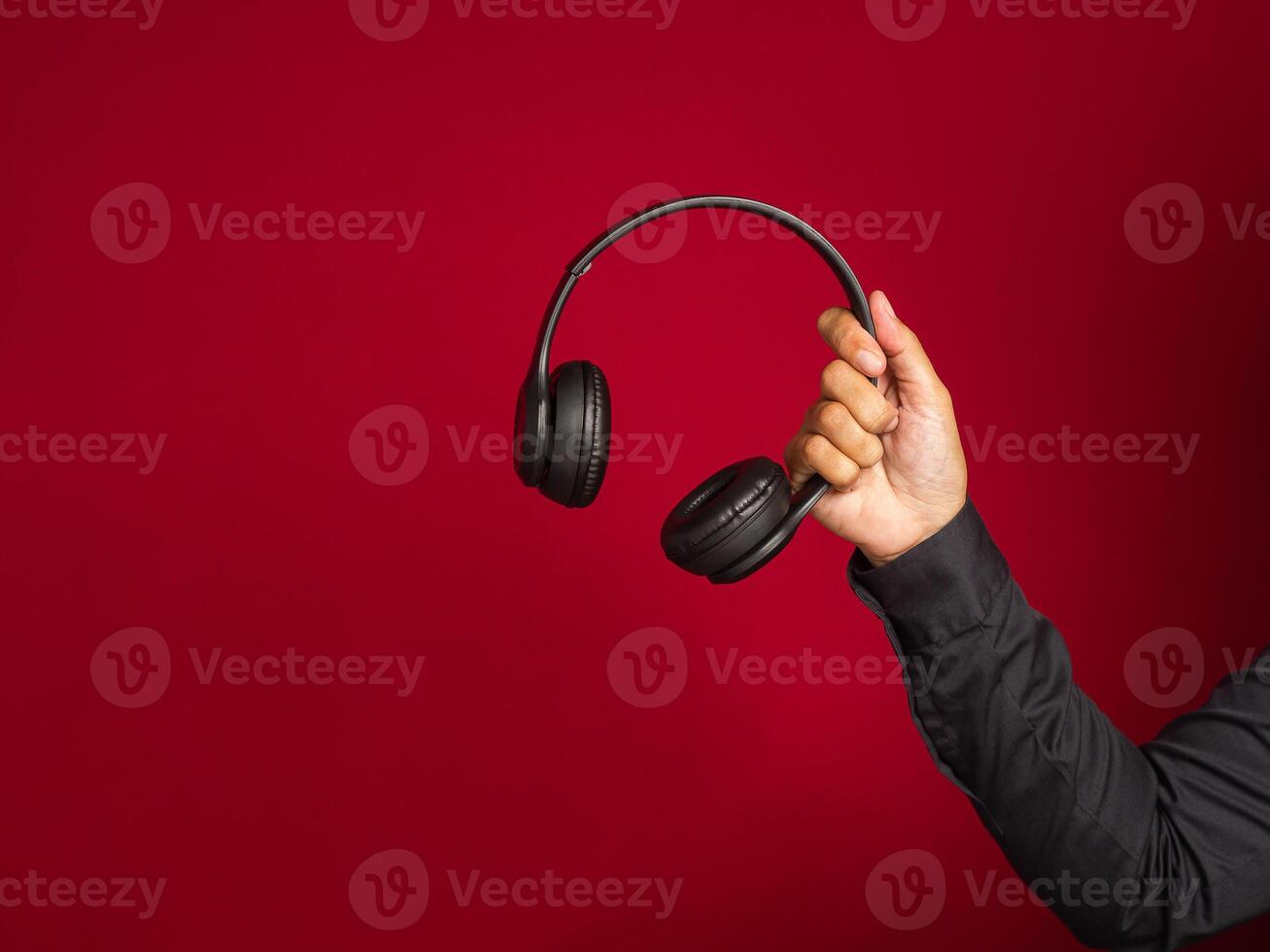 Hand holding a wireless headphone over a red background with copy space for text. Close-up photo. Music and relaxation concept photo