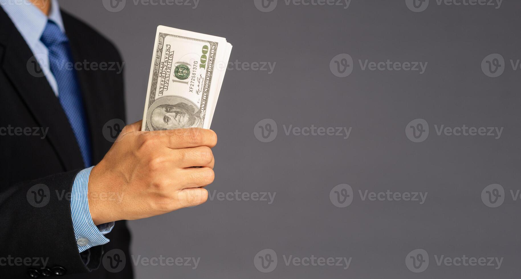 Hand of a businessman holding US dollars banknote with a gray background while standing in the studio. Close-up photo. Space for text photo