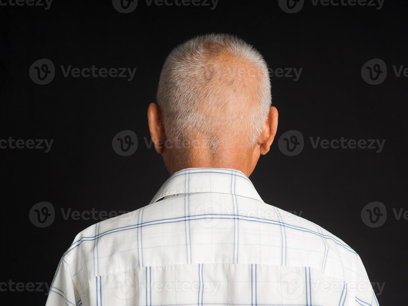Back view of a senior man in a white shirt standing on black background in the studio. Aged people and healthcare concept photo