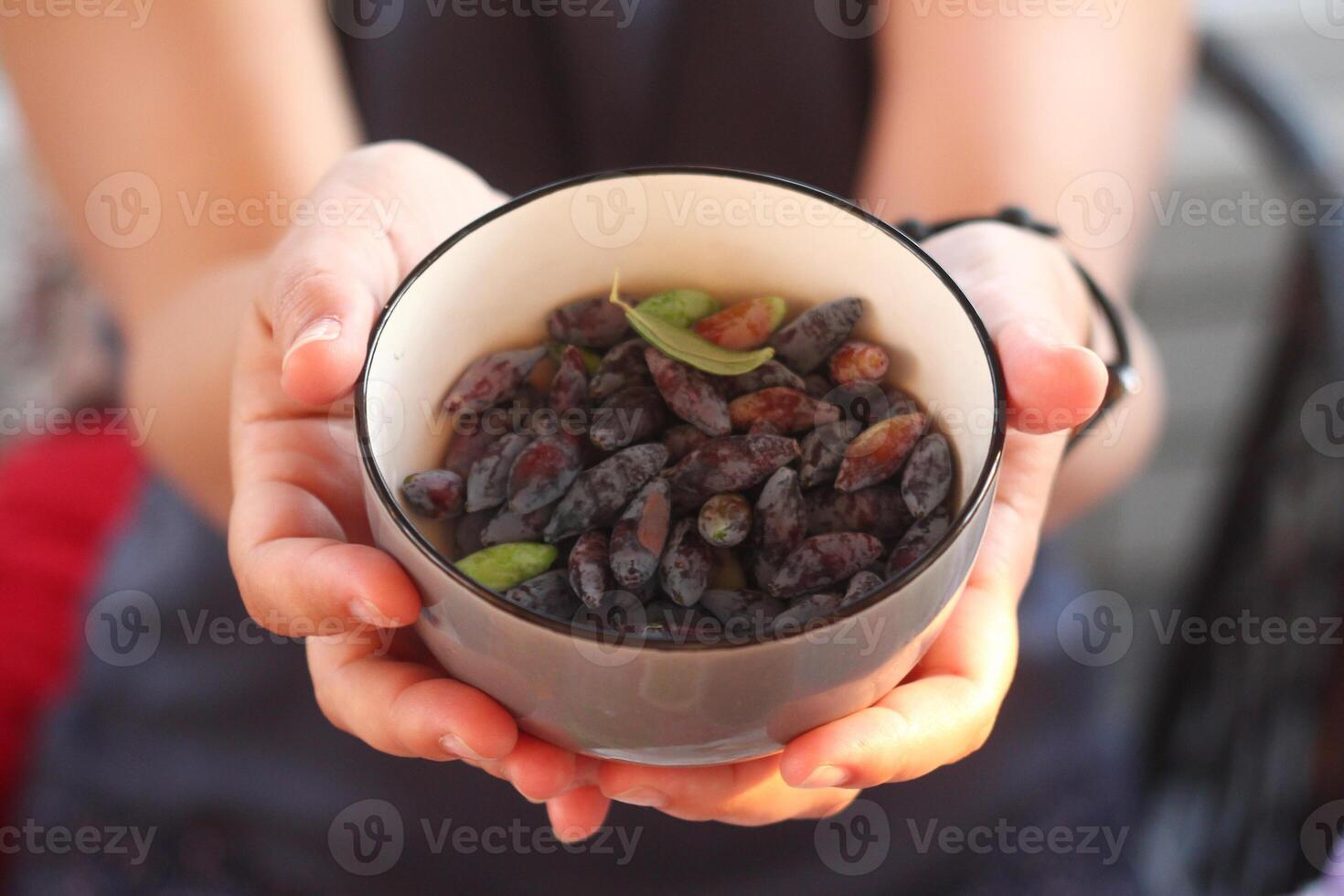 Close-up of hands holding a bowl filled with ripe fresh honeysuckle. First summer harvest. photo