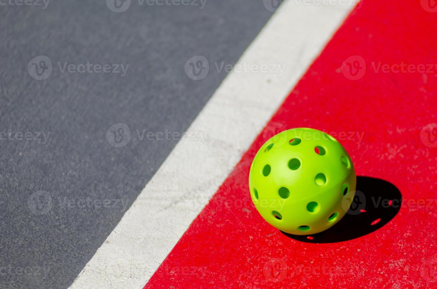 Pickleball ball isolated on red and grey court, racket sports concept photo