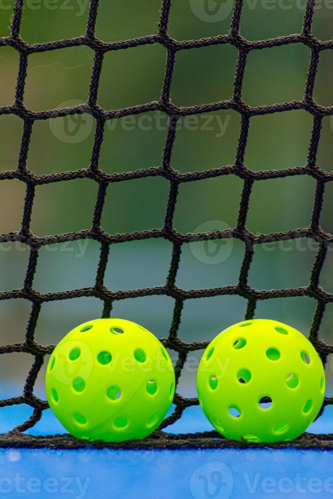 Two pickleball balls in front of a blue court net photo