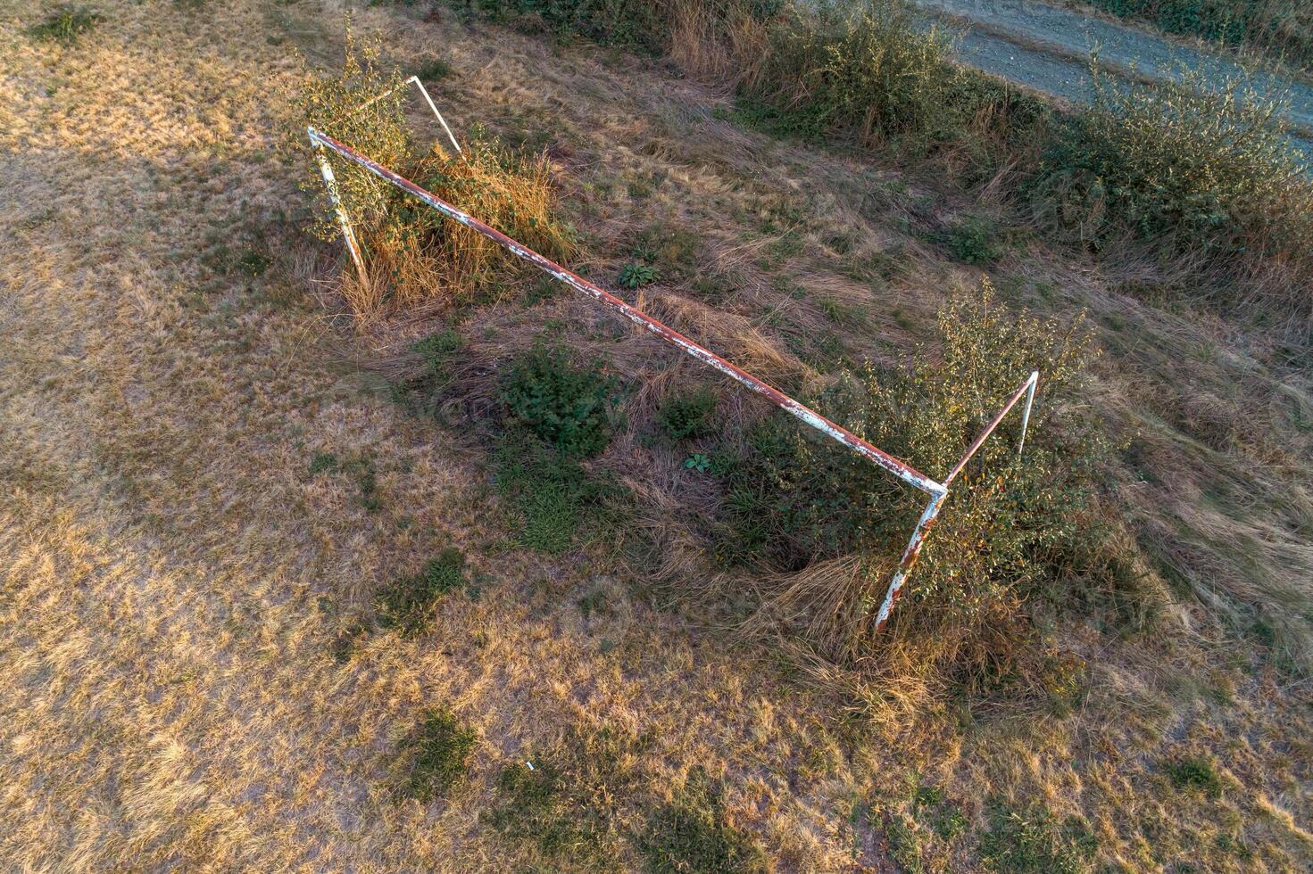 a goal of an abandoned football pitch covered by weeds, aerial top view from a drone photo
