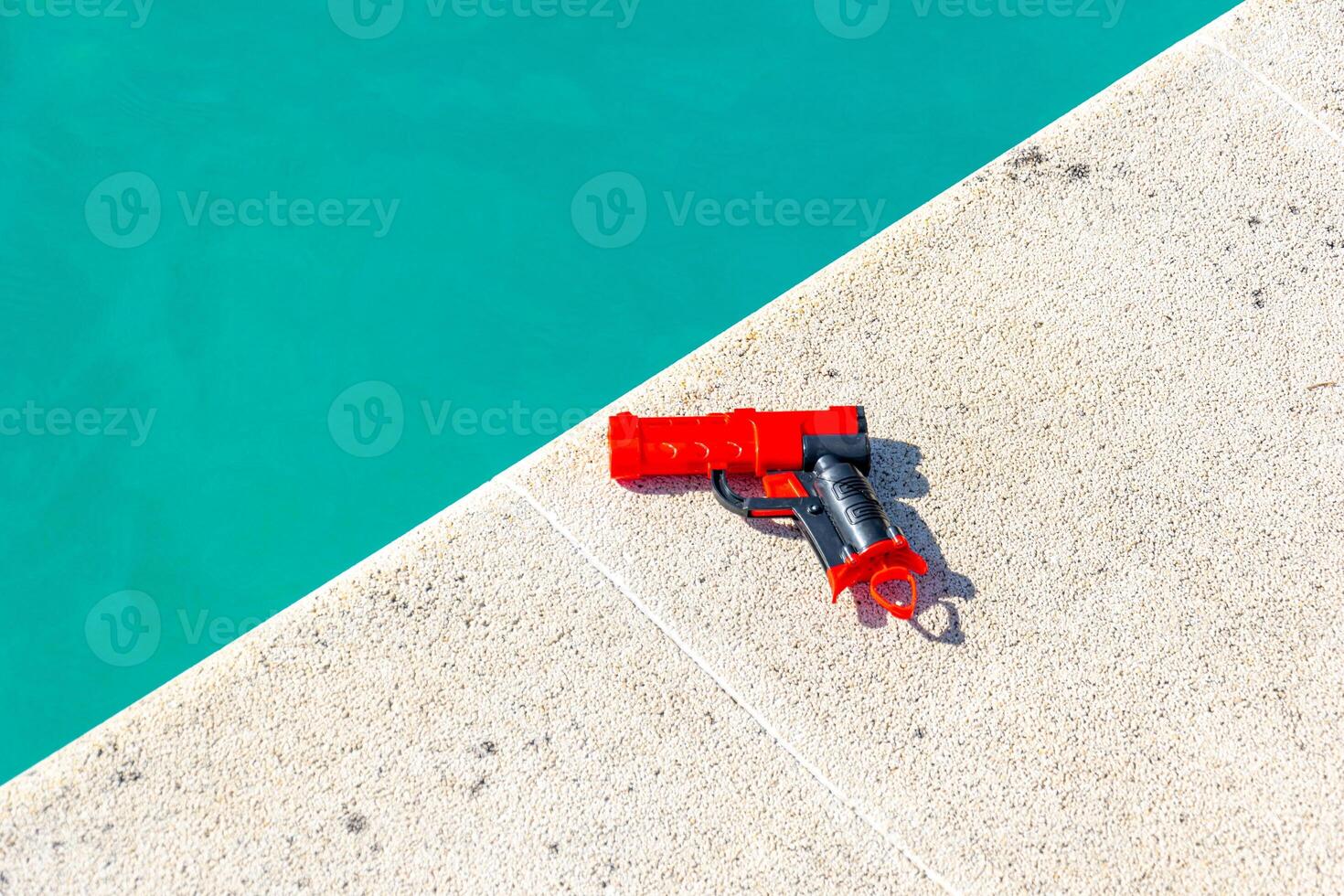 red plastic gun on the edge of a swimming pool in summertime, holidays concept photo